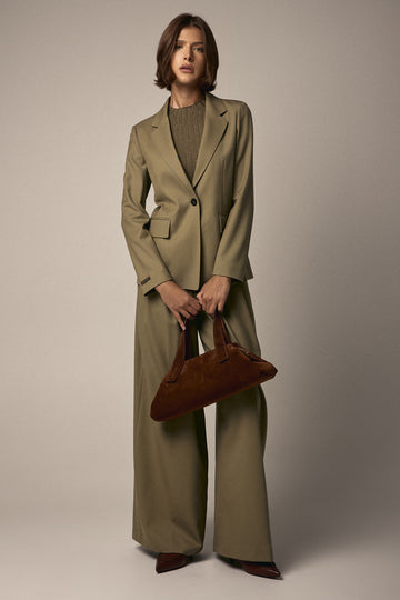 Person wearing a beige suit holding a brown handbag against a plain background