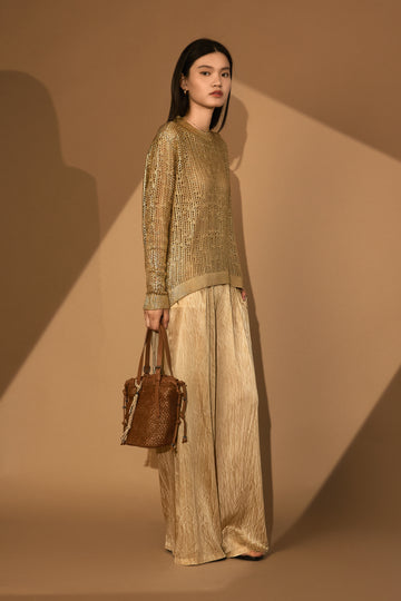 Woman in a hand painted laminated pullover and beige plazzo Touser, holding a brown leather handbag against a brown background