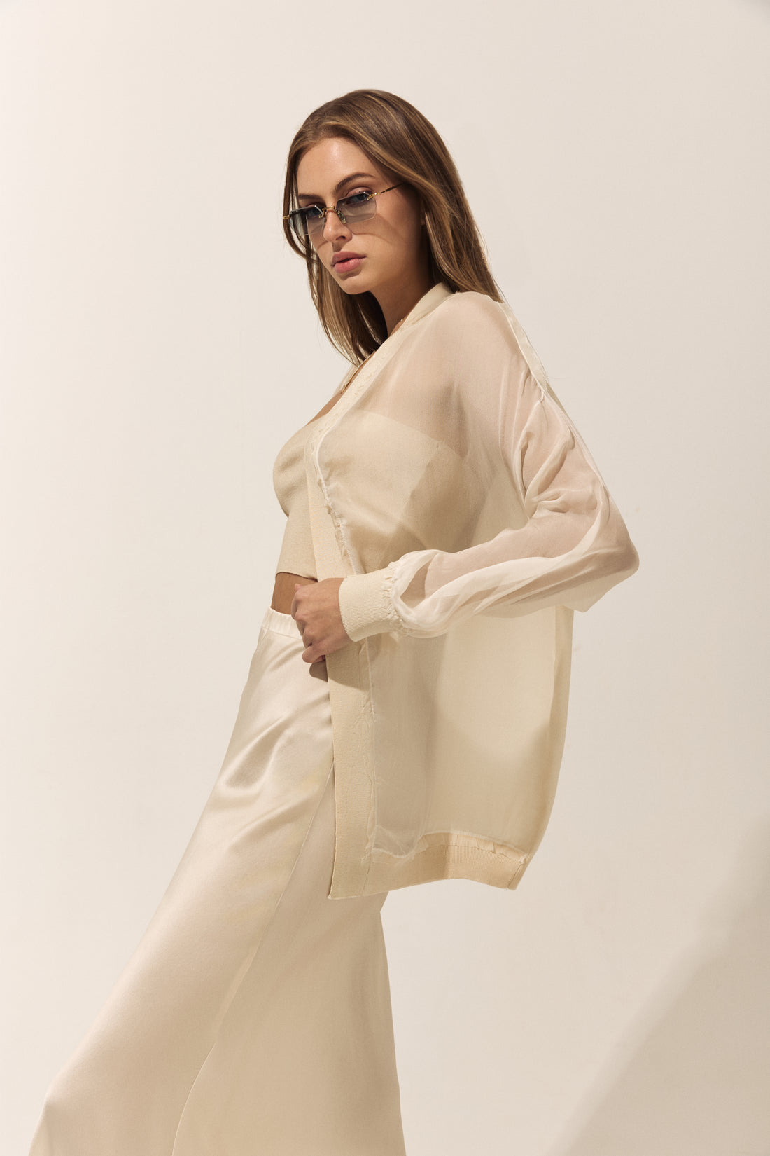Woman wearing a beige outfit with a matching cardigan on a plain background
