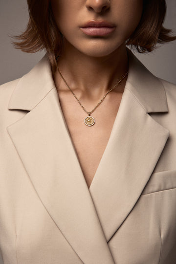 Close-up of a person wearing a beige blazer and gold necklace with a pendant.
